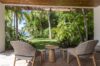 Covered patio at a St Barts villa with woven chairs overlooking lush tropical gardens and palm trees