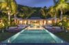 Evening view of a luxury St Barts villa with illuminated infinity pool, palm trees, and elegant outdoor lounge areas.