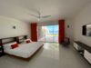 Modern bedroom in a St Barts villa with king bed, red curtains, flat-screen TV, and sliding doors opening to ocean views.