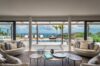 Chic living room in a St Barts villa opening onto a pool terrace with loungers, palm trees, and ocean views beyond.