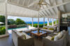 A beautiful outdoor patio with comfortable sofas and armchairs that overlooks an infinity-edge pool, with the vast, sparkling blue ocean and tropical trees in the background.