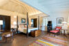 a large, bright bedroom with a four-poster king-size bed, high vaulted ceilings, and a comfortable seating area.