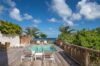 “Poolside deck at St Barts villa with lounge chairs, tropical greenery, and ocean horizon
