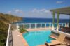 Outdoor pool with clear turquoise water, sun loungers, and panoramic ocean views from a villa terrace.