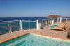 Outdoor pool with clear turquoise water, sun loungers, and panoramic ocean views from a villa terrace.”