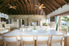 Spacious open-plan villa with high wooden ceiling, stone feature wall, large dining table, and ocean-view terrace in St Barts rental