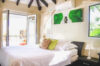 Sunlit bedroom in a St Barts villa with beamed ceiling, glass doors to terrace, and tropical garden views.