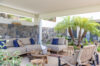 Covered outdoor lounge in St Barts villa with stone walls, tropical plants, and cozy seating.