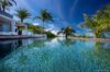 Sparkling infinity pool at a St Barts villa surrounded by palm trees and modern white architecture under a vivid blue sky.