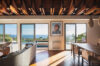 Contemporary living and dining area in a St Barts villa with ocean views through sliding glass doors and exposed wooden beams overhead.