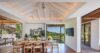Bright dining room in a St Barts villa with wooden table, vaulted ceiling, and sliding doors opening to garden and terrace views.