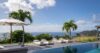 Infinity pool at a St Barts villa with white sunbeds, umbrellas, and palm trees overlooking the Caribbean Sea and hillsides.