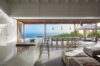Open-plan kitchen and dining area in a St Barts villa with bar seating, long dining table, and panoramic ocean views through sliding doors.