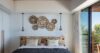 Elegant bedroom in a St Barts villa with woven wall décor, pendant lights, and sliding doors opening to a terrace view.