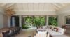 Open-plan living and dining area in a St Barts villa with vaulted ceiling, wooden dining table, and views of tropical gardens.