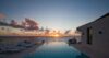 Infinity pool at a St Barts villa reflecting a vibrant Caribbean sunset with loungers lining the terrace by the sea.