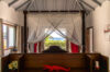 Romantic bedroom in a St Barts villa with canopy bed, ocean view, and tropical light through windows.