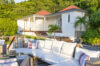 Sunlit terrace of a St Barts villa with white cushioned seating facing tropical gardens and hillside.