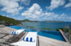 Infinity pool with wooden deck and sun loungers overlooking the Caribbean Sea and rolling green hills in St Barts.