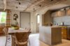 Rustic-style kitchen in a St Barts villa with wooden beamed ceiling, stone island, and dining table with wicker chairs.
