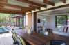Covered terrace with wooden dining table opening to pool deck and airy living room in St Barts villa rental.
