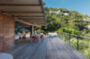 Spacious wooden terrace at a St Barts villa with dining area, lounge seating, and hillside views.