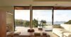 Sunlit living room in a St Barts villa with minimalist décor, wooden table, and ocean views through glass doors.