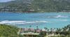 Aerial view of St Barts villa resort with red rooftops, tennis court, and turquoise bay surrounded by green hills.