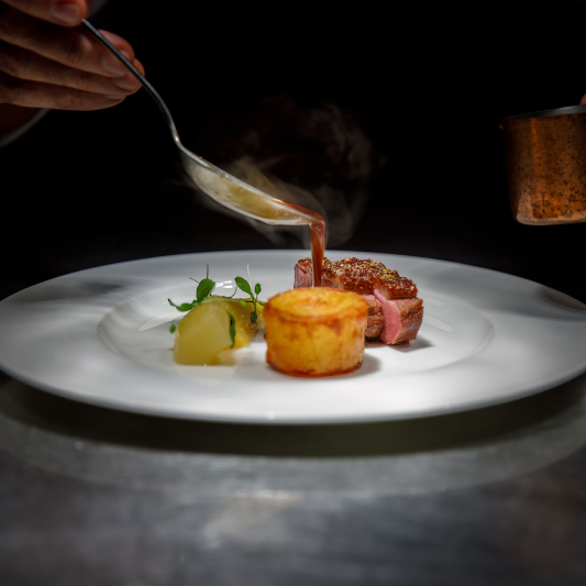 St. Barts villa chef artfully plating anniversary dinner with seared meat, potato preparation, and rich sauce.