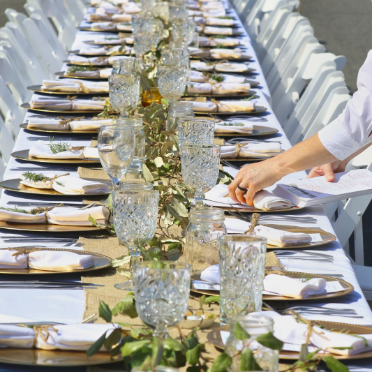 Staff preparing outdoor dining table with white tablecloth.