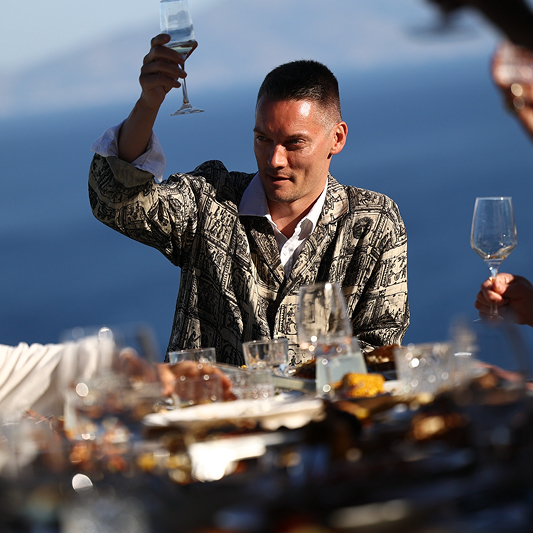 Birthday celebration toast with guest holding champagne glass at fine dining table with ocean view and elegant glassware.