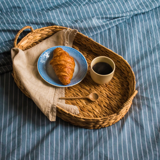 Breakfast in bed with golden croissant on light blue plate and black coffee in cream mug on woven wicker tray at St. Barts villa.