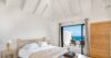 Bright bedroom in a St Barts villa with vaulted white ceiling, natural wood bed frame, and terrace doors opening to ocean views, ideal for luxury villa rentals