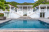 Swimming pool with deck facing white colonial-style villa surrounded by green hills in St Barts villa rental
