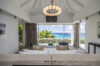 Elegant villa living room with modern chandelier, white sofas, and floor-to-ceiling window overlooking the Caribbean Sea in St Barts rental
