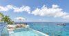 Infinity pool at a luxury St Barts villa overlooking the Caribbean Sea with yachts anchored in the turquoise bay and lounge chairs under a sun umbrella