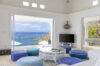 Bright living room in a St Barts villa with blue ottomans, white interiors, and panoramic ocean views of anchored yachts in the Caribbean