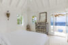 Bright white bedroom in a luxury St Barts villa with ocean view terrace and French doors opening to a shaded lounge area