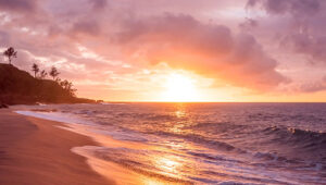 Sunset over a sandy beach with gentle waves and a partly cloudy sky in St. Barts