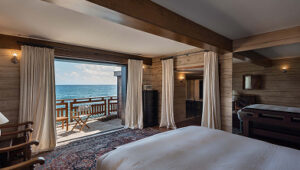 Cozy bedroom with wooden walls, ocean view balcony, and warm natural light.