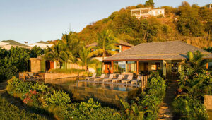 Villa on hillside with lush greenery, palm trees, and sunlit lounge chairs in Grand Cul-de-Sac.