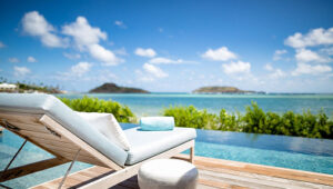White lounge chair by infinity pool overlooking ocean and islands.