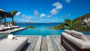 Infinity pool overlooking ocean with lounge chairs on wooden deck.