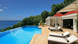 Infinity pool with lounge chairs on a terrace overlooking the ocean beside a villa.