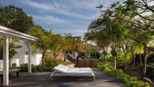 Sunlit outdoor deck with white lounge chairs surrounded by lush tropical greenery.
