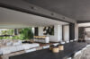 Spacious open-plan living area with a long dining table, modern white sofa, and sleek kitchen overlooking lush greenery.