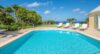 A sunlit pool, loungers, and sea in the distance