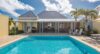 Tropical-style villa with a bright blue pool, palm trees, and outdoor seating
