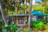 Charming tropical villa with teal roofs, surrounded by palm trees and lush greenery, featuring an outdoor dining deck