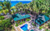 Tropical beachfront villa with green-roofed bungalows, a private pool, and palm trees overlooking the turquoise sea